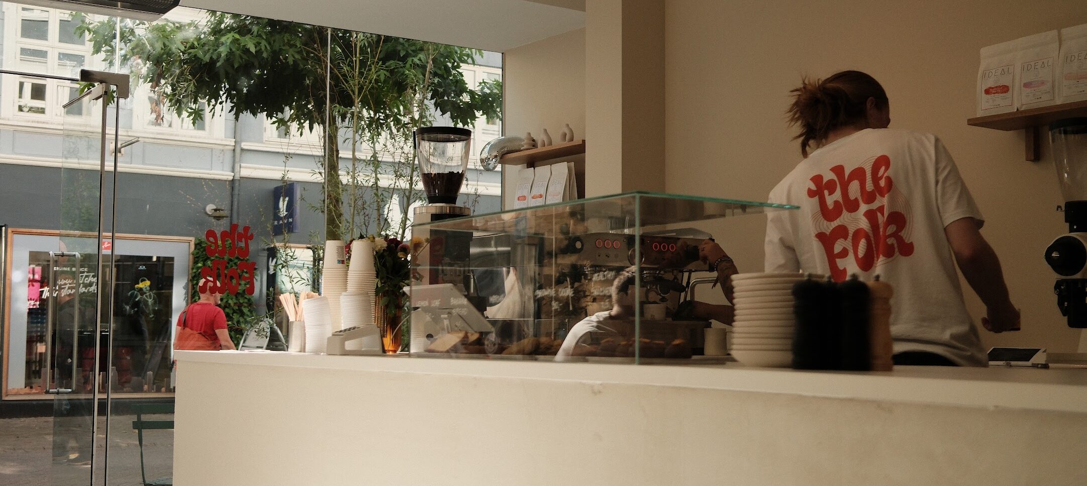 coffee shop bar with barista from back wearing the folk merchandise